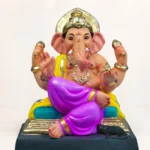 eco-friendly Ganesha idol in Padmasana pose, featuring a prominent red Maratha turban, sitting outdoors against a vibrant green garden backdrop.