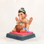 eco-friendly clay Ganesha idol sitting elegantly inside a large, ornate golden urli bowl filled with red flower petals.