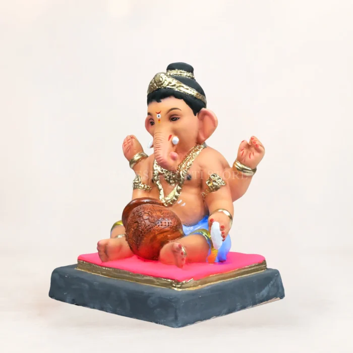 eco-friendly clay Ganesha idol sitting elegantly inside a large, ornate golden urli bowl filled with red flower petals.